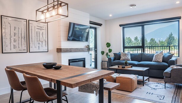 A modern living room with a wooden dining table, a sofa, and a TV mounted on the wall. - Glades and Green by Revelstoke Vacations (Revelstoke)