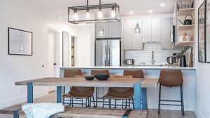 A modern kitchen with a central island, stainless steel appliances, and a hanging light fixture. - Glades and Green by Revelstoke Vacations (Revelstoke)