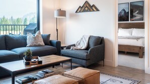 A modern living room with a sofa, armchair, coffee table, and a view of a mountain landscape through a large window. - Glades and Green by Revelstoke Vacations (Revelstoke)