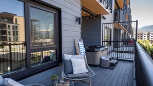 A balcony with a wicker chair, a small table with a glass, and a grill. - Glades and Green by Revelstoke Vacations (Revelstoke)