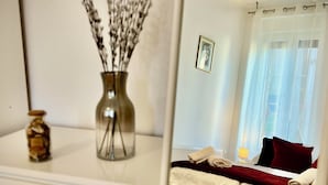 Una camera da letto con un letto, un comodino, un vaso con rami, una foto incorniciata e un lampadario.