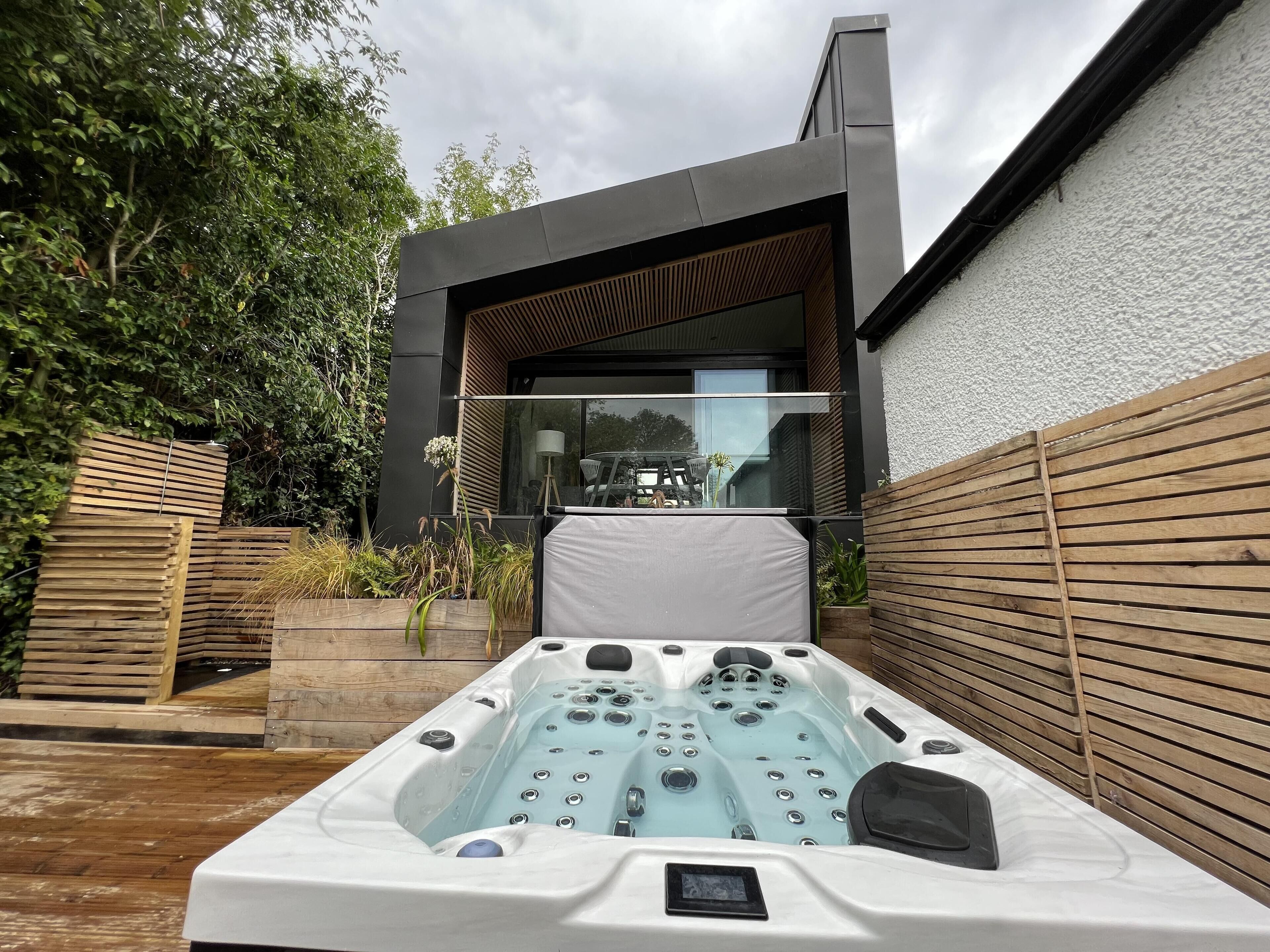 A modern outdoor hot tub with a control panel, surrounded by wooden decking and a wooden fence.