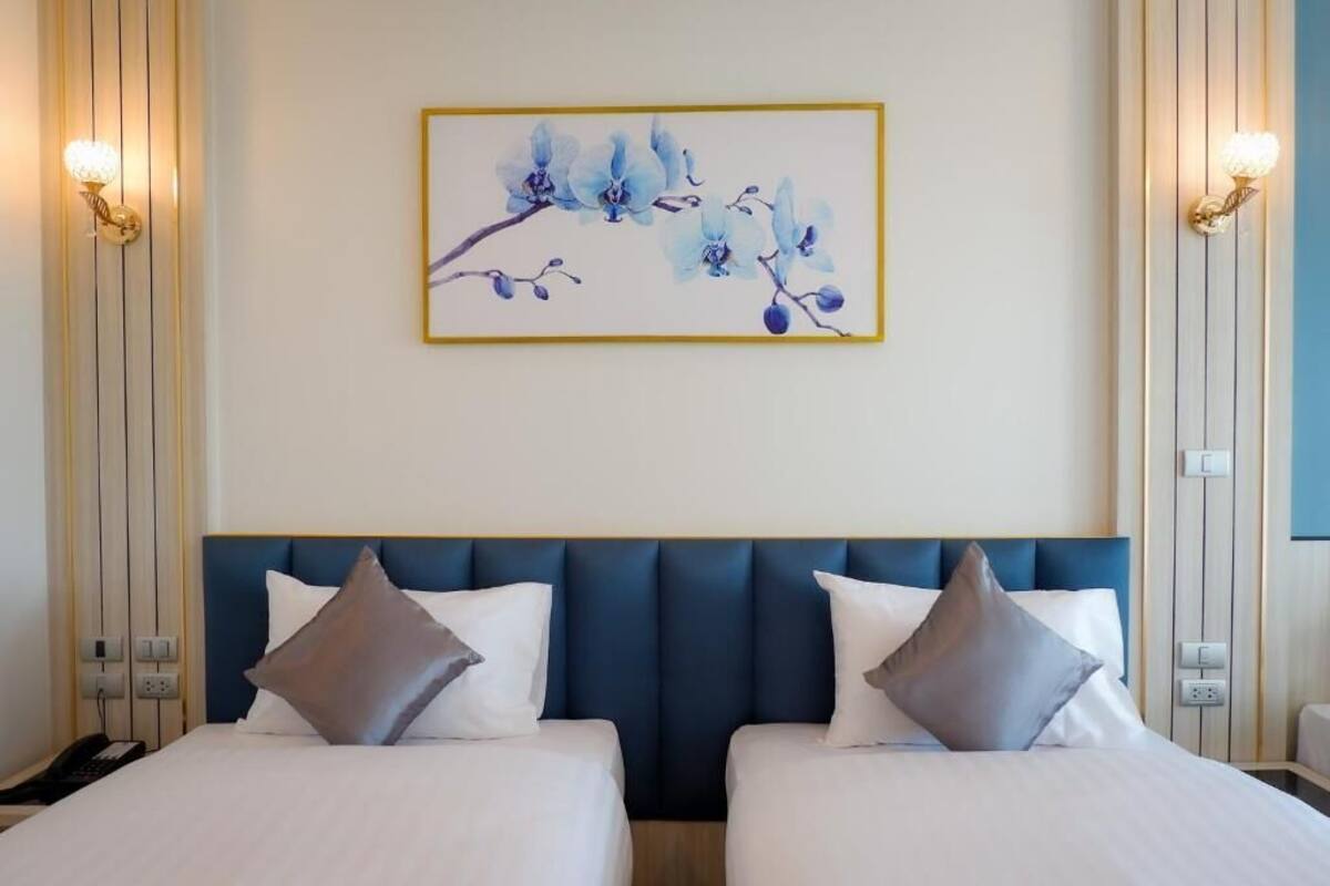 A hotel room with two beds, a large blue headboard, and a framed floral artwork on the wall.