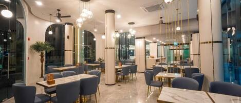 Un interior de restaurante moderno con mesas redondas, sillas azules e iluminación colgante.