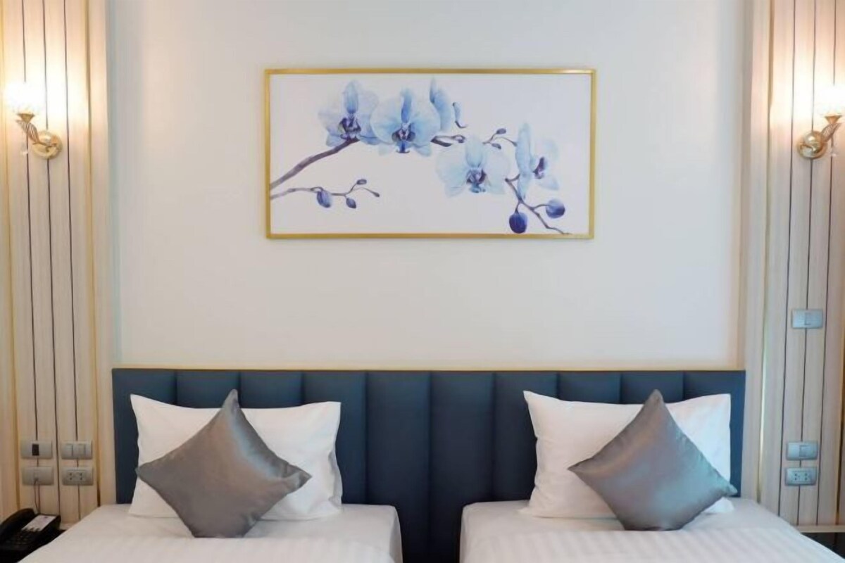 Une chambre d’hôtel avec deux lits, une tête de lit bleue et une œuvre d’art encadrée représentant des fleurs bleues, accrochée au mur.