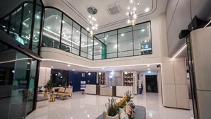 A modern hotel lobby with a reception desk, seating area, and a glass-enclosed upper level. - Poolrada Boutique Hotel (Thep Krasattri)