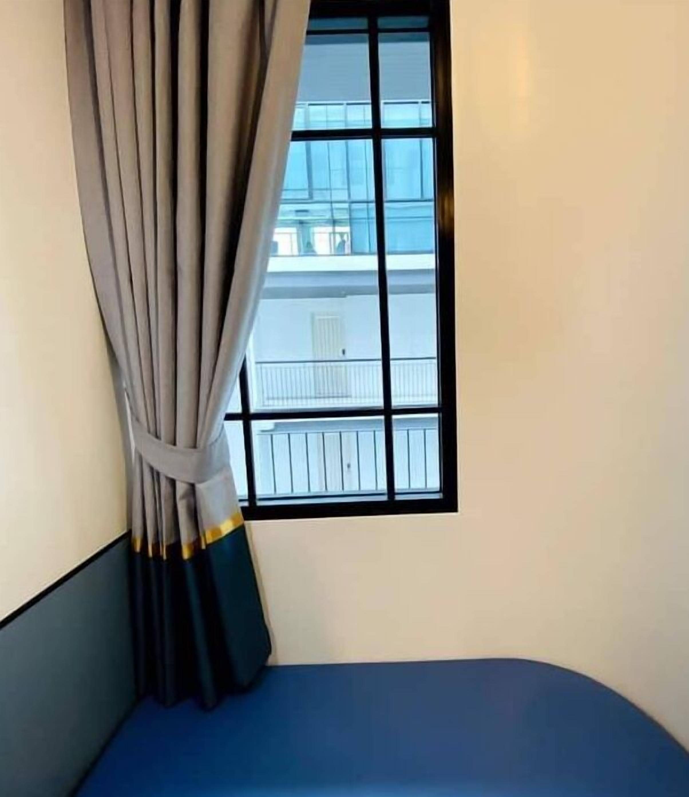 A room with a window, a curtain, and a blue bed.