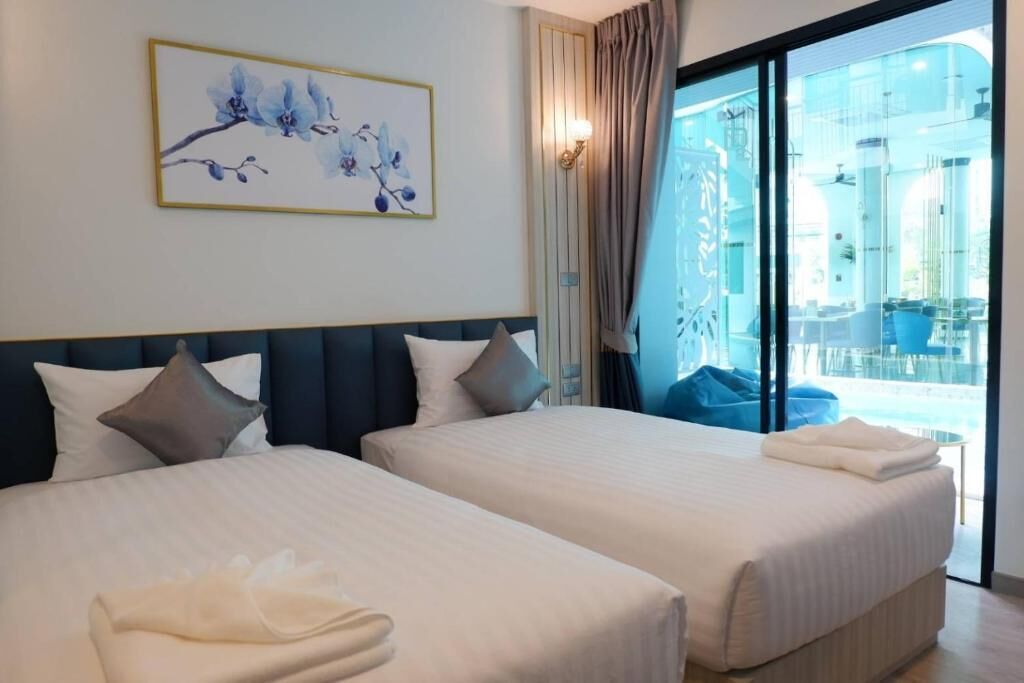 A hotel room with two beds, a large window with a view of a pool and outdoor seating, and a framed floral artwork on the wall.