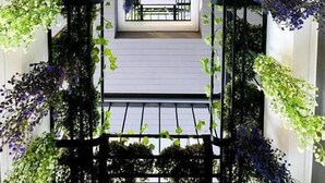 A corridor with a view of a room through a window, surrounded by greenery and a black metal gate. - Poolrada Boutique Hotel (Thep Krasattri)