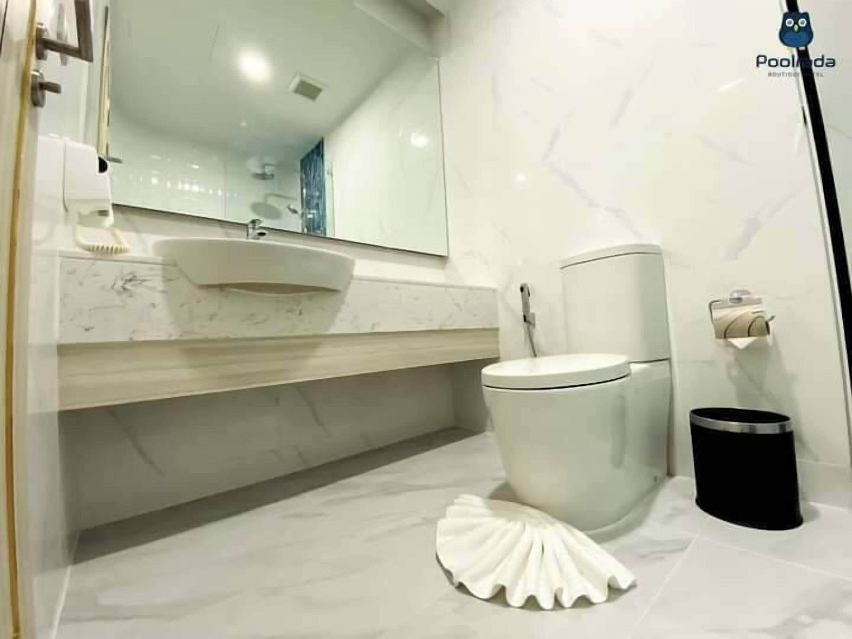 A modern bathroom with a white sink, mirror, toilet, and a decorative white object on the floor.