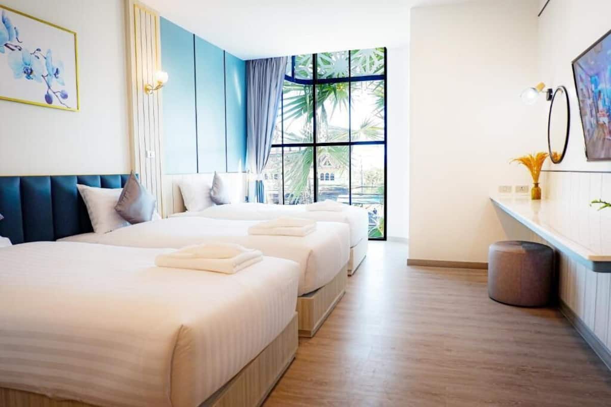 A hotel room with two beds, a large window with a view, a desk, and a trash bin.