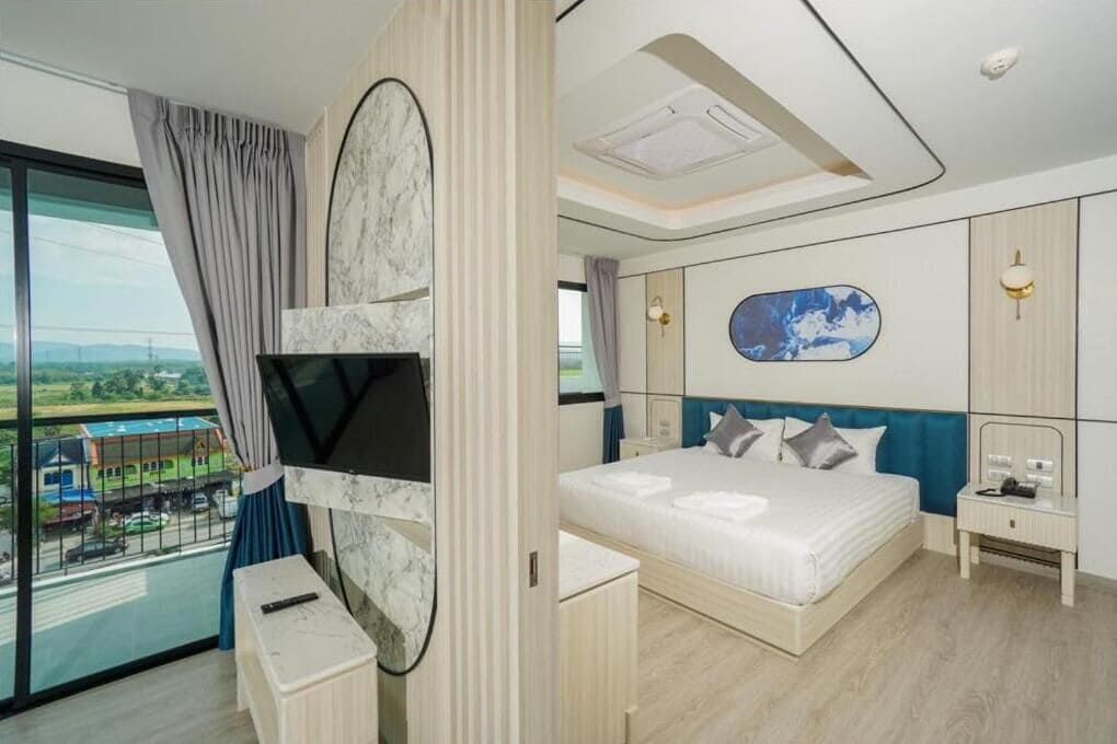 A modern hotel room with a large bed, a TV mounted on the wall, a balcony with a view, and a small desk.