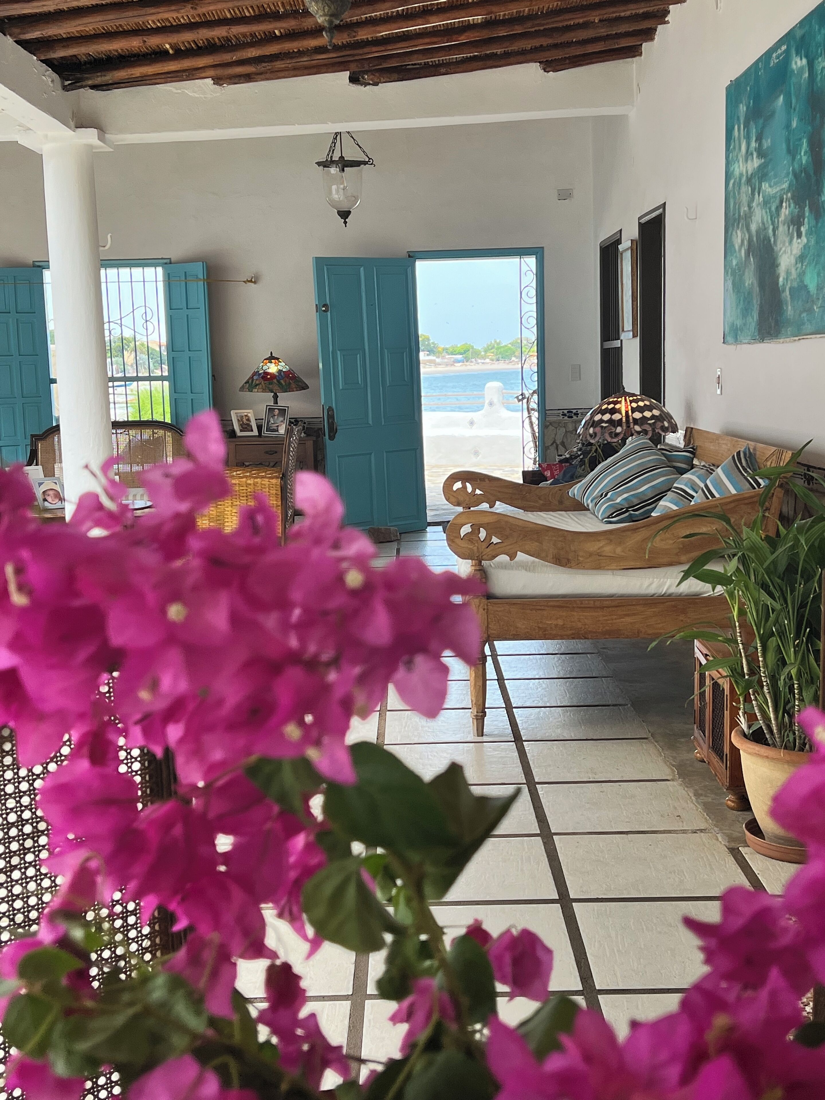 A room with a wooden bed, a view of the sea, and a large window with blue shutters.
