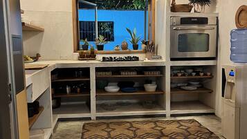 A compact kitchen with a built-in oven, a water dispenser, and a window with a view of greenery.