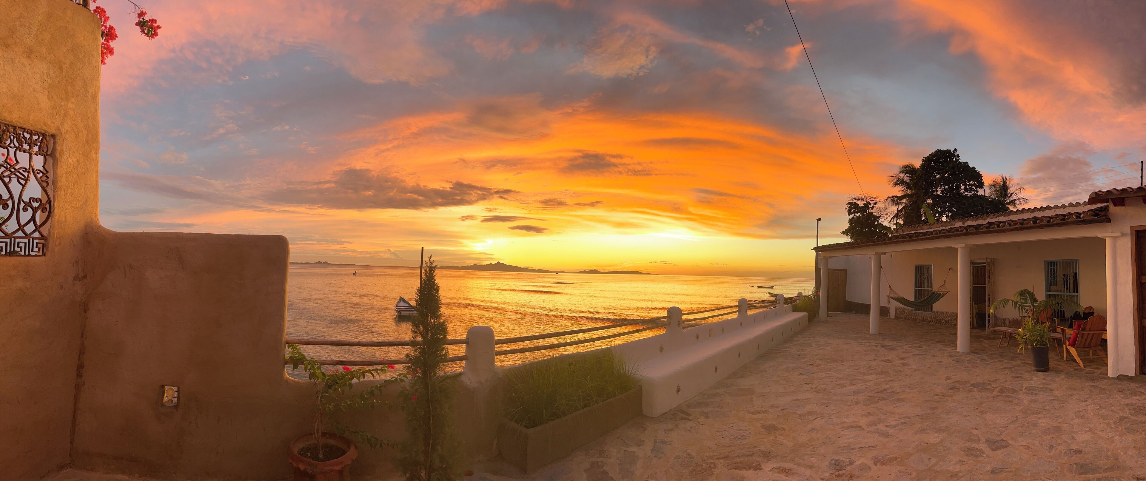 Vista costera con un atardecer, una playa arenosa y un edificio con balcón con vista al mar.