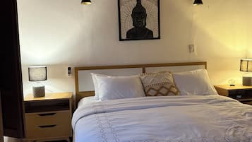 Une chambre avec un lit en bois, du linge de lit blanc, une statue de Bouddha fixée au mur, des lampes de chevet et une table de chevet avec une lampe.