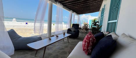 A covered outdoor seating area with a view of the beach, a ceiling fan, and a table with decorative items.