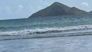 A beach with waves, pebbles, and a mountain in the background.