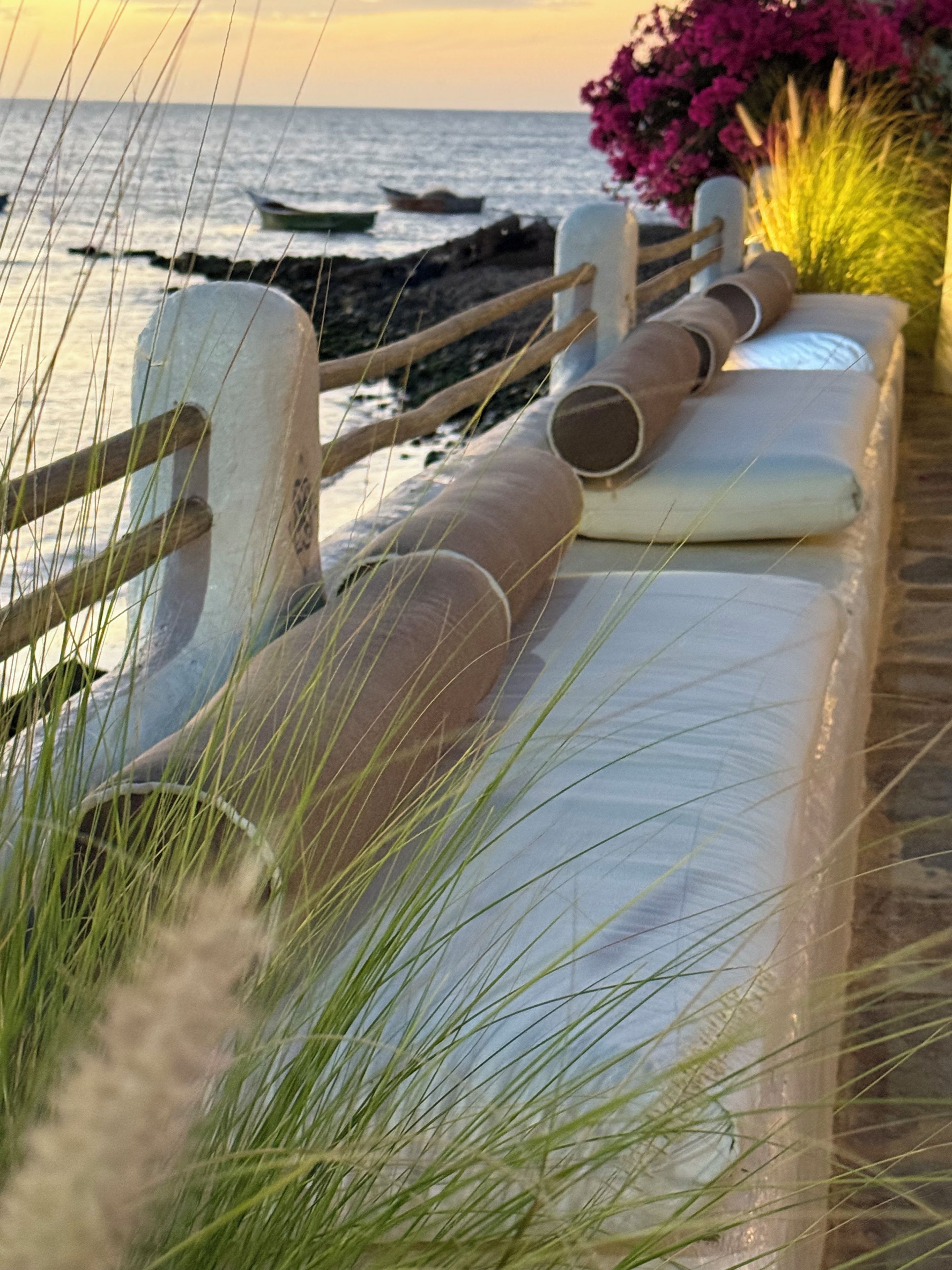 Une vue sur la côte avec une balustrade en bois, une rangée d’objets cylindriques et une étendue d’eau en arrière-plan.