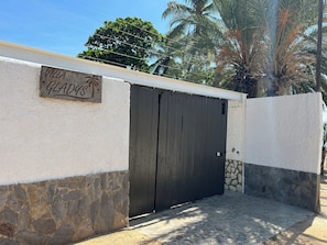 Una villa llamada "Villa Gladys" con un portón de madera oscura, muros de piedra y una palmera al fondo.