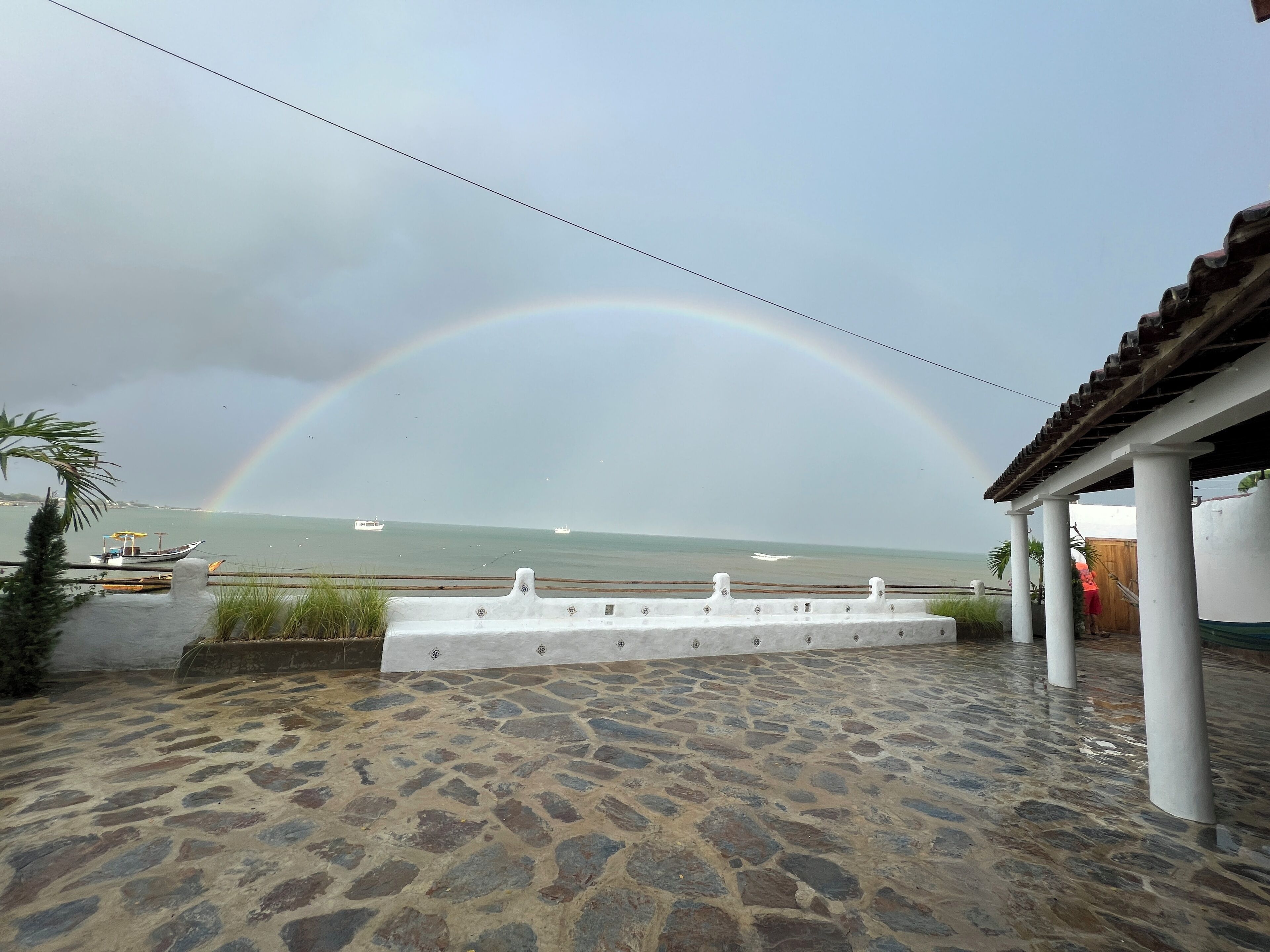 A stone-paved patio with a view of the sea and a rainbow.