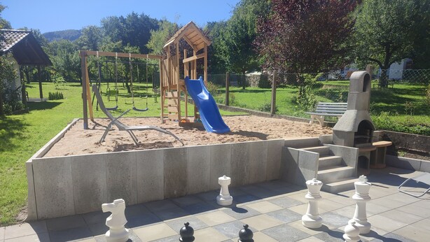 Un terrain de jeux avec un toboggan et des balançoires, un jeu d’échecs et un espace barbecue.