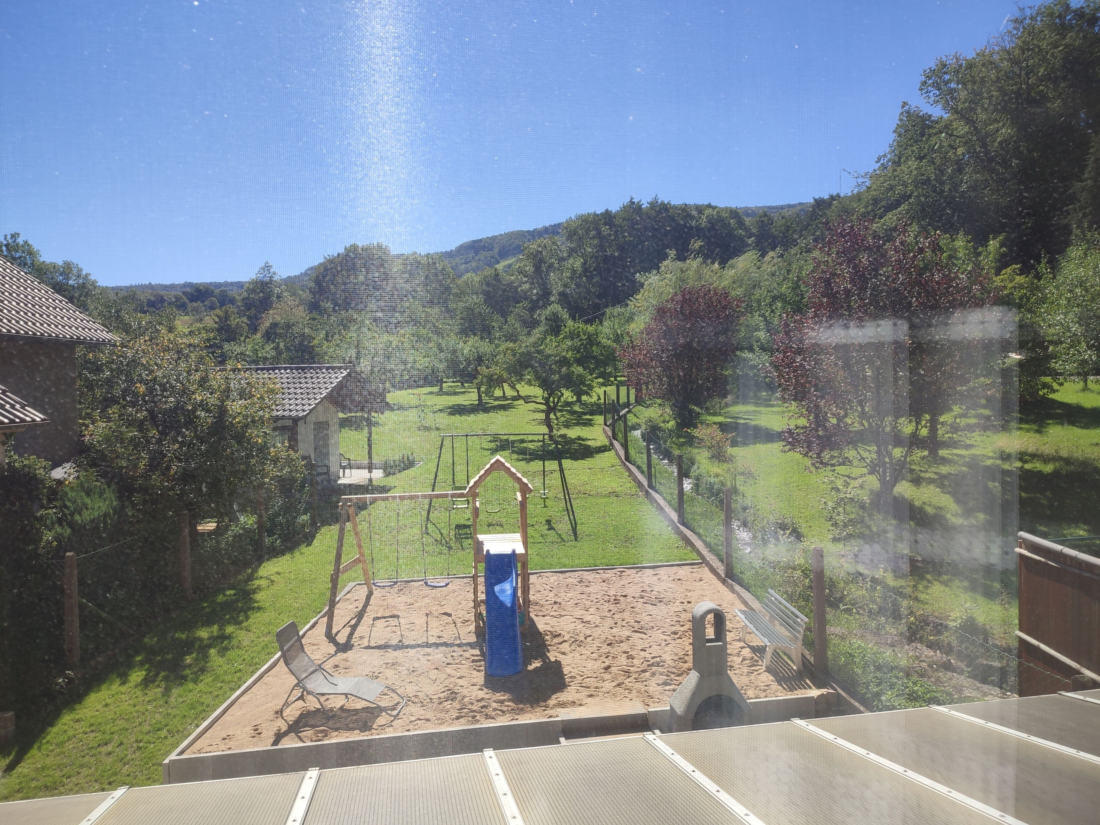 A view of a backyard with a sandy play area, a swing set, and a wooden bench.