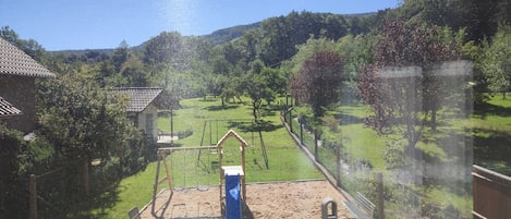 A view of a backyard with a sandy play area, a swing set, and a wooden bench.