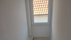Un escalier étroit avec une rampe en bois, une fenêtre en haut et une vue sur l’extérieur par cette fenêtre.