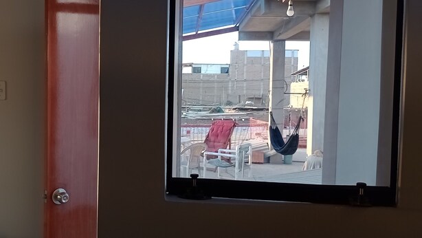 A room with a window overlooking a balcony with outdoor furniture. - Travelers' House  (Huanchaco)