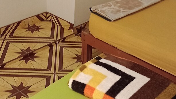 Een kamer met een bed, een houten bankje, een kapstok en een kamerbreed tapijt met een patroon.