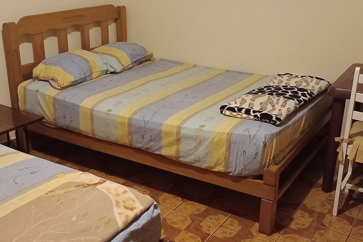 Ein Schlafzimmer mit zwei Einzelbetten, einem Holzkopfende, einer gemusterten Bettdecke, einem leopardenprinten Kissen und einem kleinen Holzstuhl.