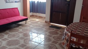 A room with a red sofa, a checkered table, patterned floor tiles, a door, and a curtain. - Travelers' House  (Huanchaco)