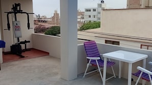A balcony with a white table and purple chairs, overlooking a cityscape with buildings and a water tank in the background. - Travelers' House  (Huanchaco)