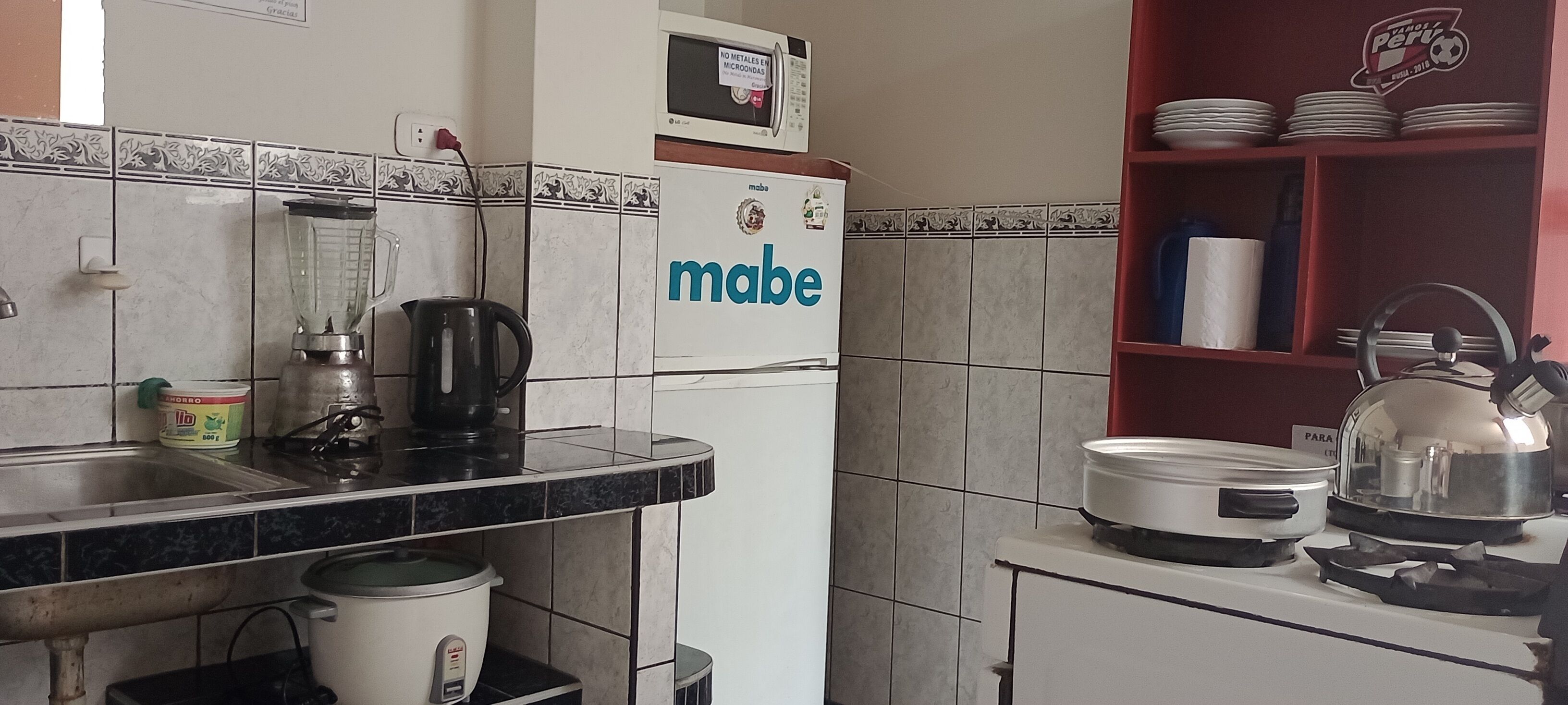 Eine Küche mit Kühlschrank, Herd, Wasserkocher und verschiedenen Küchenutensilien.