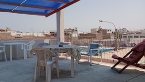 A rooftop terrace with a table and chairs, a pool, and a view of the cityscape. - Travelers' House  (Huanchaco)
