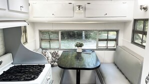 Interior compacto de una caravana con kitchenette, una mesa de comedor y una zona de estar con vistas al exterior.