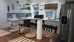 Een moderne keuken met een roestvrijstalen koelkast, een magnetron en een spoelbak. Er staan twee stoelen bij een tafel met placemats.
