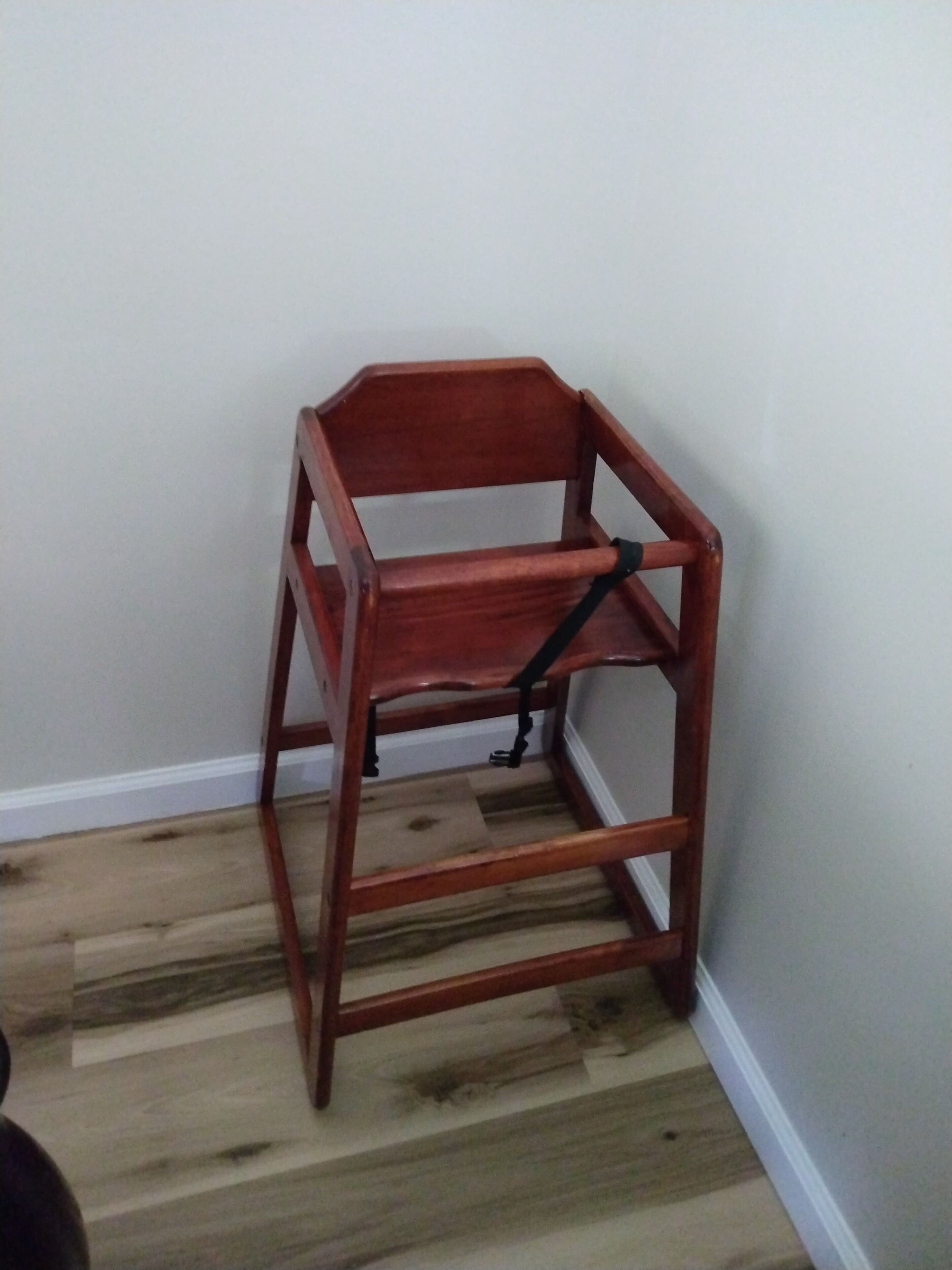 Une chaise en bois, dotée d’un dossier et d’accoudoirs, est placée contre un mur, au-dessus d’un plancher en bois.