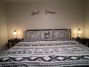 A neatly made bed with patterned bedding, two bedside lamps, and a wall with the words 'Sweet Dreams' above it.