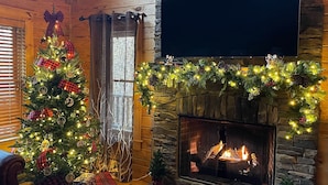 A cozy living room with a fireplace, a Christmas tree, and festive decorations. - Cabin log home w view, hot tub, game room. Community pool 4 bedroom Sleeps 10-12 (Deep Gap)