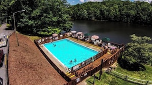 A rectangular swimming pool surrounded by a wooden deck with lounge chairs and umbrellas. - Cabin log home w view, hot tub, game room. Community pool 4 bedroom Sleeps 10-12 (Deep Gap)