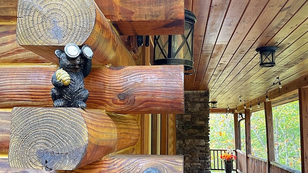 A log cabin interior with a wooden floor, a stone fireplace, and a bear figurine. - Cabin log home w view, hot tub, game room. Community pool 4 bedroom Sleeps 10-12 (Deep Gap)