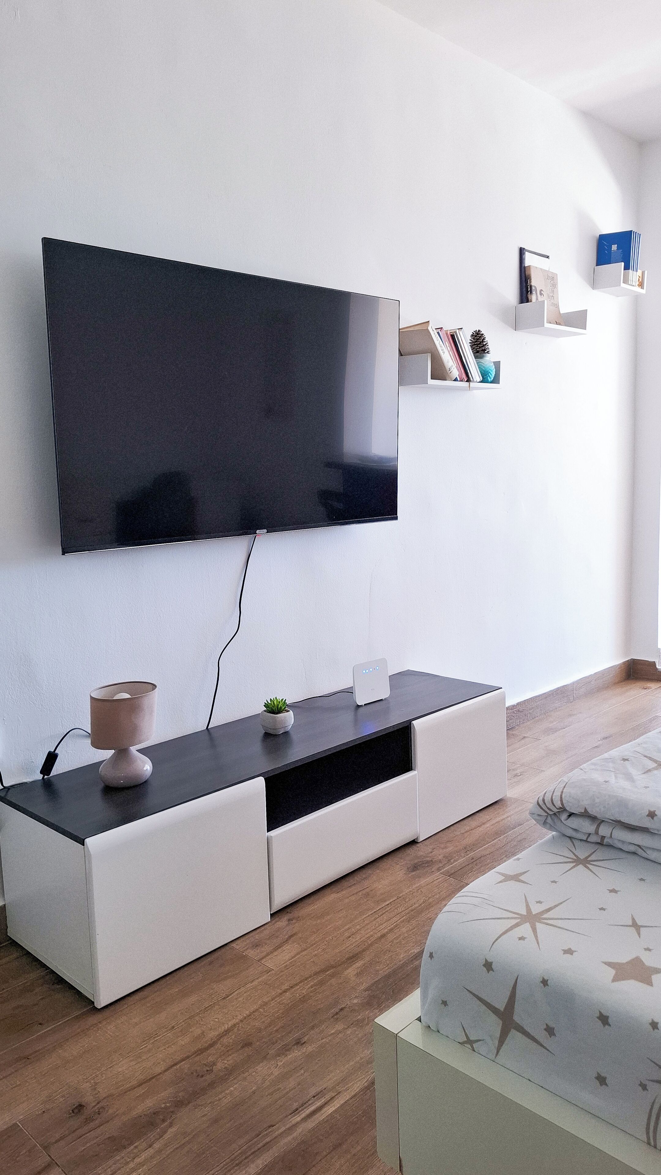 A modern living room with a flat-screen TV mounted on the wall, a minimalist entertainment unit with drawers, a small plant, and a decorative item on the unit.
