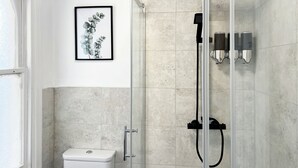Uma casa de banho moderna com cabine de duche envidraçada, sanita e impressão botânica emoldurada na parede.