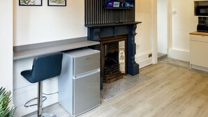 Cozinha moderna com frigorífico embutido, um banco de bar, uma TV de ecrã plano montada acima de uma lareira e um pequeno armário com micro-ondas.
