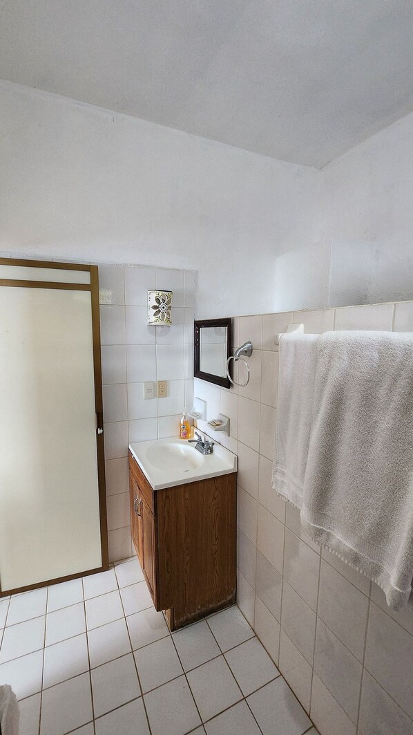 Un baño con tocador de madera, un espejo, toallero y zona de ducha.