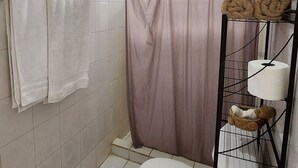 Ein kleines Badezimmer mit Toilette, einer Duschvorhang und einem Ablagebereich mit Handtüchern und Toilettenartikeln.