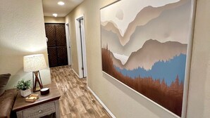 Ein Flur mit Holzboden, einem großen Landschaftsbild an der Wand, einer Lampe und einem Schrank.