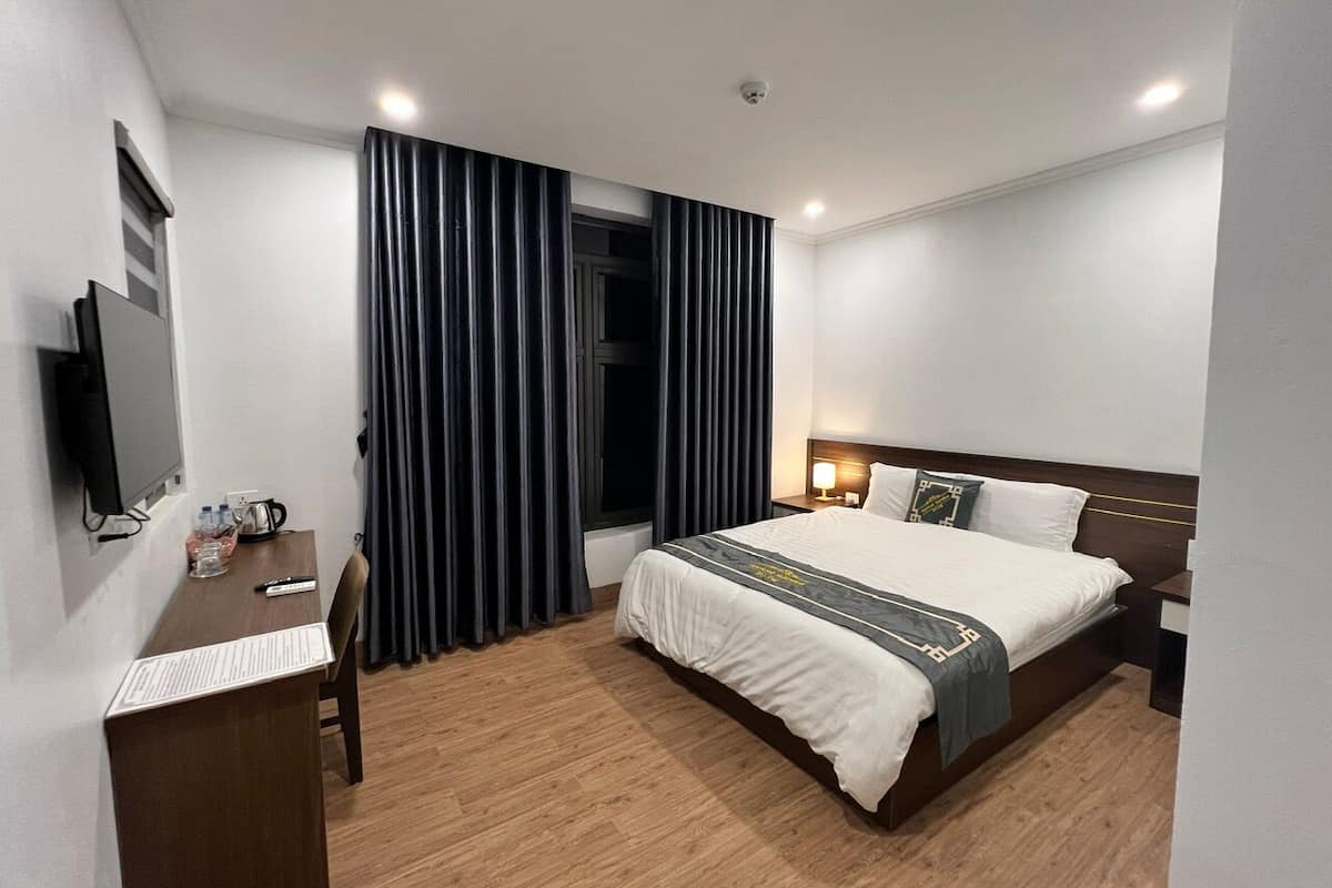 A hotel room with a bed, a desk, a chair, a TV, and a window with curtains.